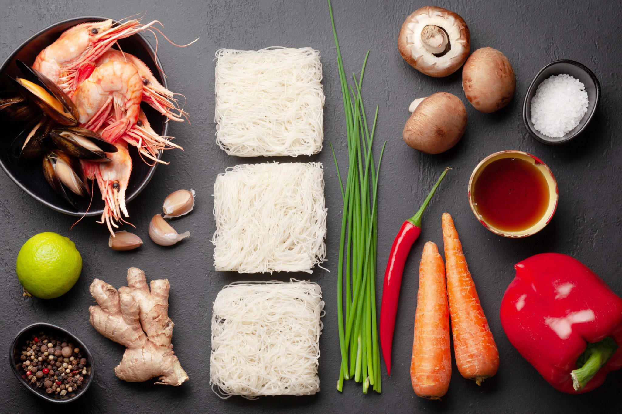 Ingredients for wok cooking with stir fried noodles, shrimps and vegetables on stone background. Top view flat lay
